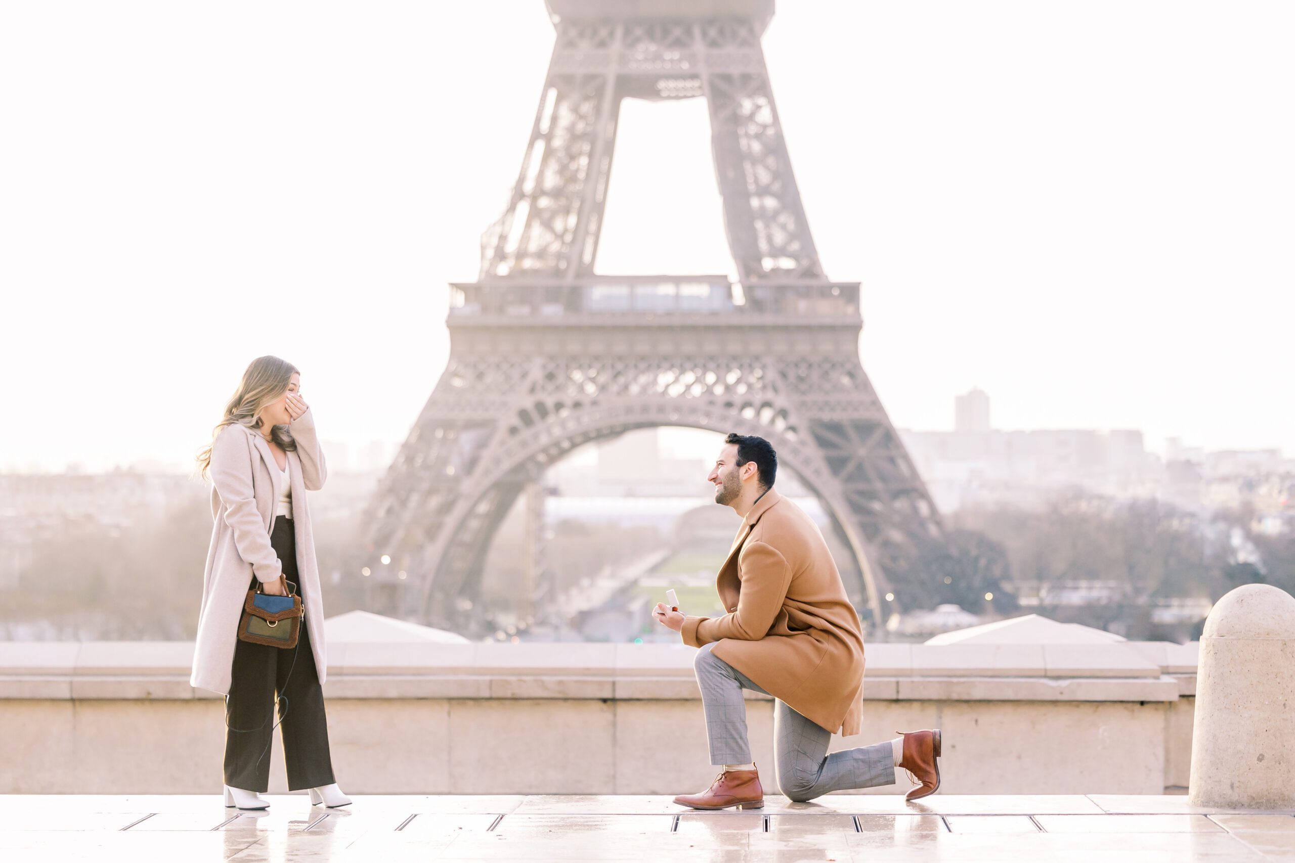 a guy down on one knee proposing to his girlfriend in front of the Eiffel Tower in Paris